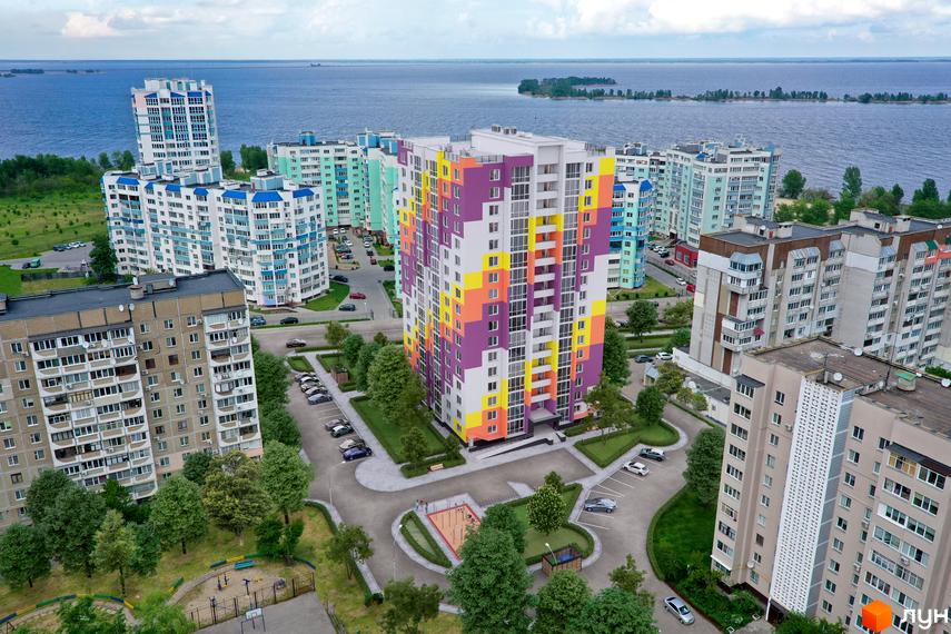 Житловий комплекс Парковий на Дніпрі з яскравим фасадом, облаштованим двором, парковкою та дитячим майданчиком біля річки.