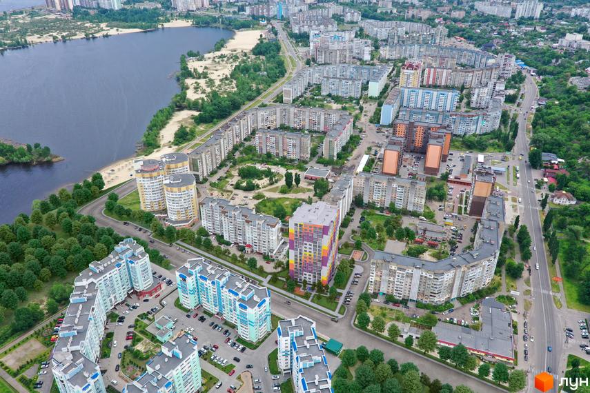 Парковий на Дніпрі: вид з висоти пташиного польоту на багатоповерхові будинки з яскравими фасадами та зелену прибудинкову територію біля річки.