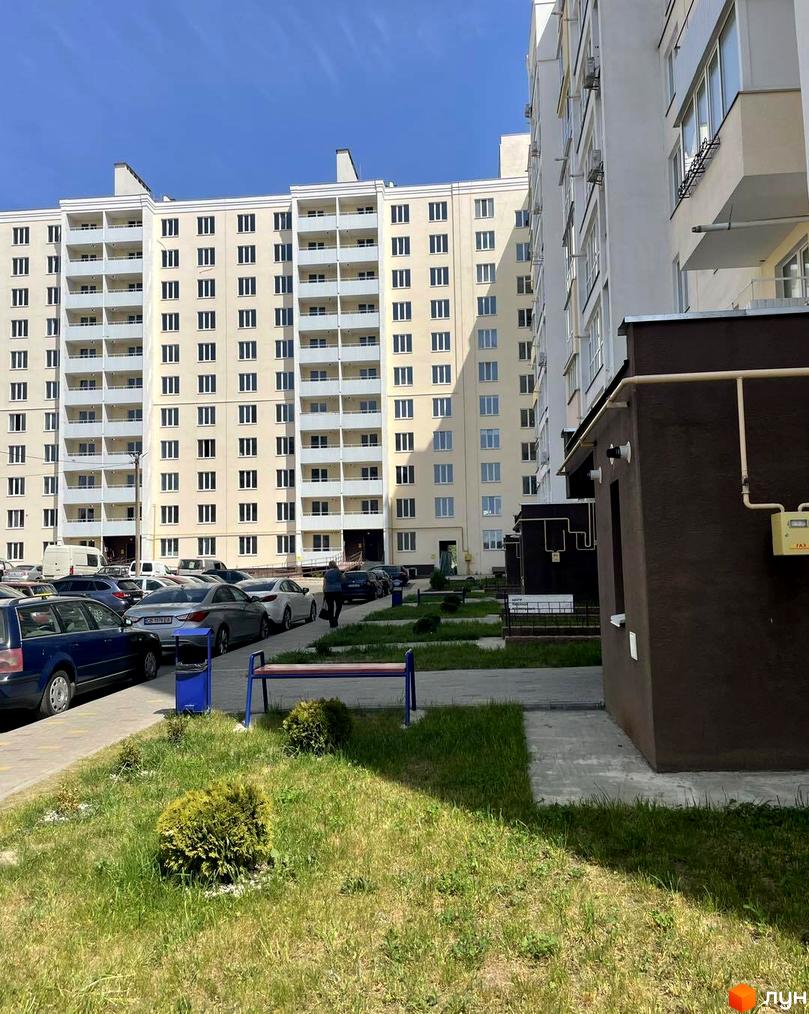 Новобудова ЖК на Масанах. Зовнішній вигляд багатоповерхових будинків з балконами та паркуванням автомобілів біля них. Прибудинкова територія з газоном та лавкою.