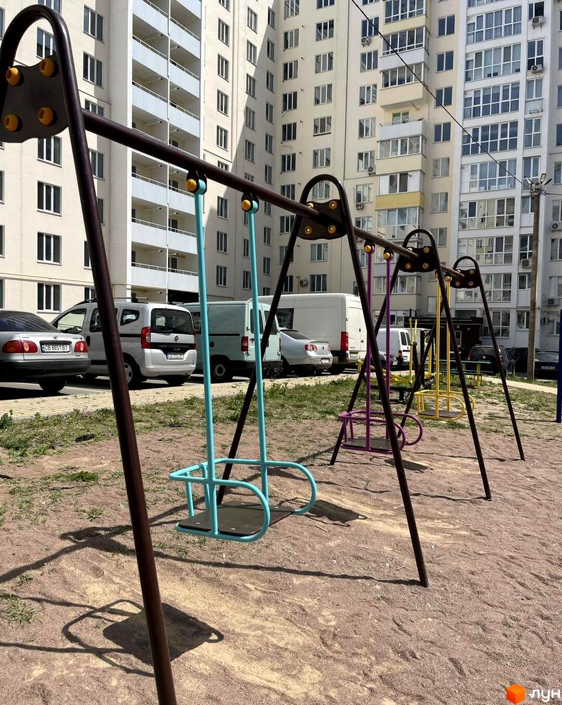 Житловий комплекс на Масанах. Дитячий майданчик з гойдалками на фоні багатоповерхових будинків.