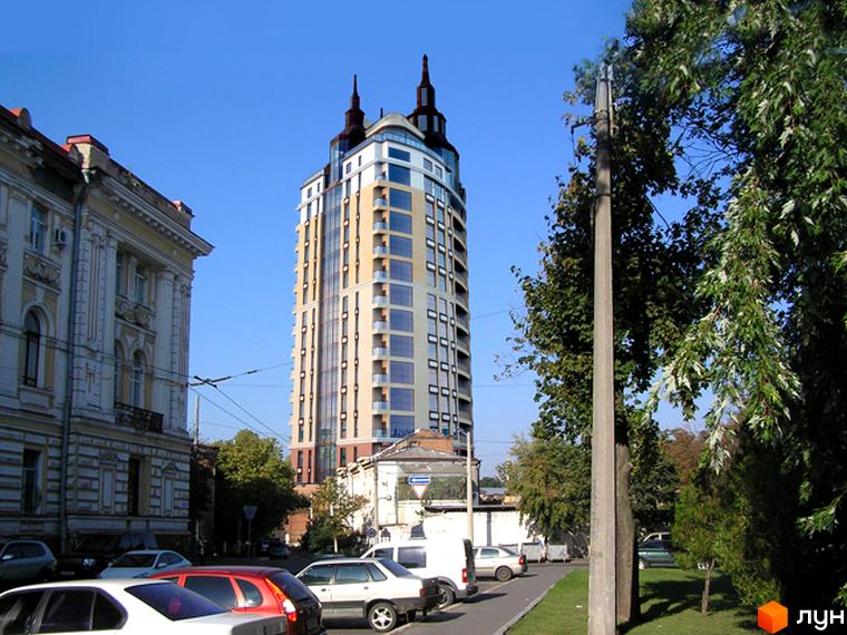 Житловий комплекс Зарічний з сучасним фасадом та прибудинковою територією, озелененою деревами та автомобілями.