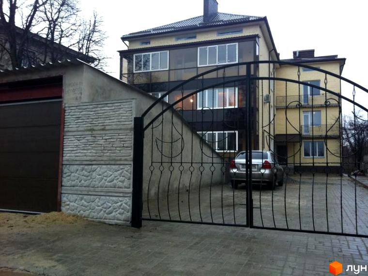 Житловий комплекс на вул. Підлісна, 15, з сучасною архітектурою та прибудинковою територією. Вид на двір з автомобілем та огорожею.