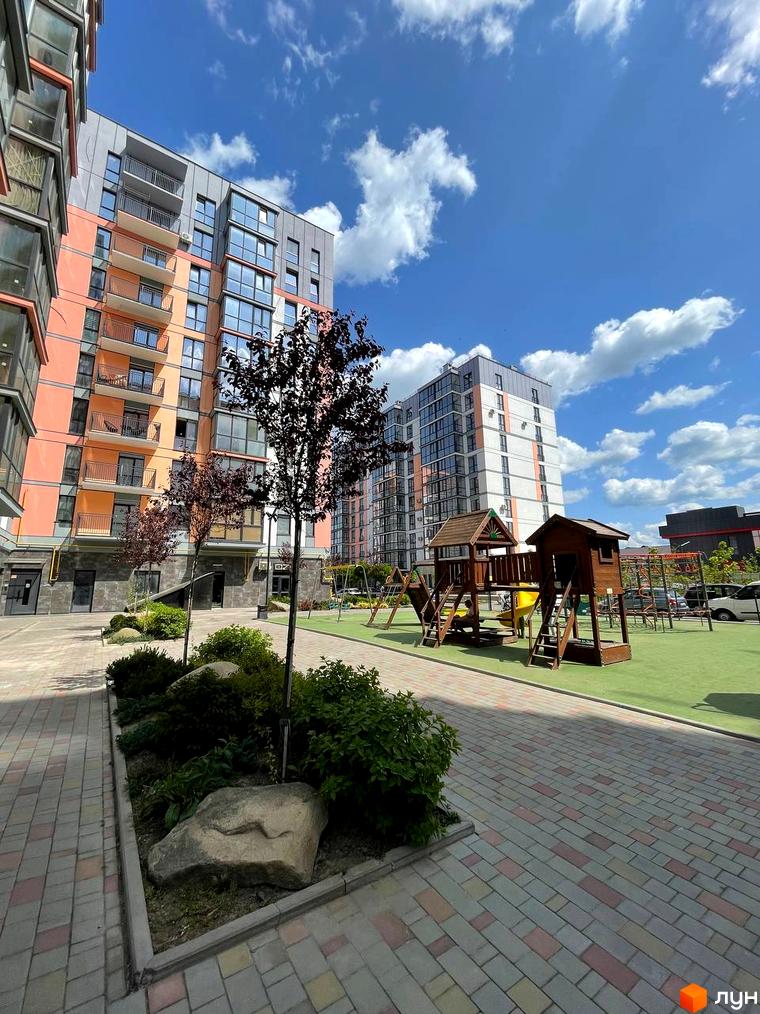 Житловий комплекс Dream Town: фасади будинків з панорамними вікнами та балконами, дитячий майданчик з дерев'яними будиночками на зеленій території.