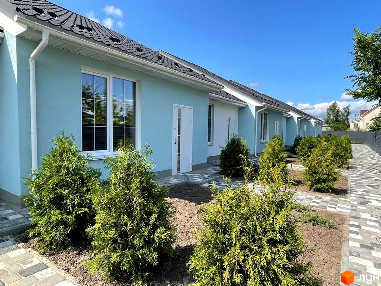 Ряд таунхаусів SMARTS з блакитними фасадами та темним дахом. Перед будинками висаджені зелені кущі та прокладена бруківка.