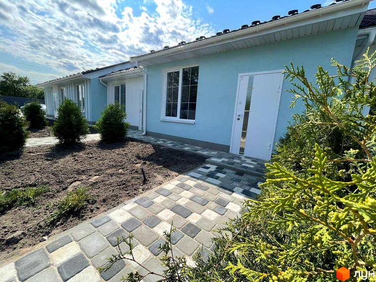 Таунхауси SMARTS: світло-блакитний будинок з білими вікнами та дверима, перед яким прокладена вимощена доріжка та висаджені молоді дерева.