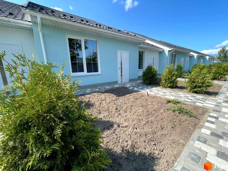 Ряд таунхаусів SMARTS зі світло-блакитними стінами, білими вікнами та темними дахами. Перед будинками доріжки з бруківки та молоді зелені насадження.