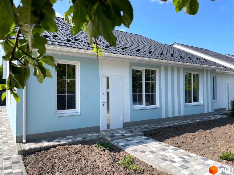 Фасад таунхаусу SMARTS світло-блакитного кольору з білими вікнами та вертикальними смугами. До входу веде вимощена доріжка.