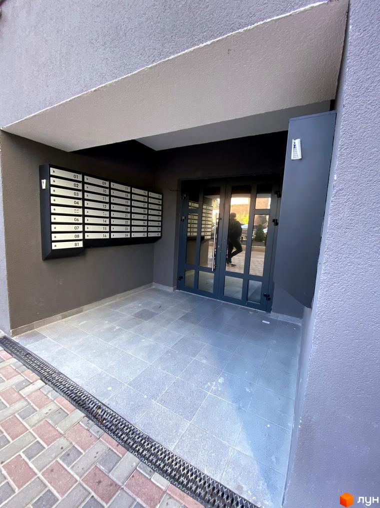 Зовнішній вигляд входу до будинку ЖК Green Life-3 з поштовими скриньками та дверима. Прибудинкова територія з плиткою та решіткою для стоку води.