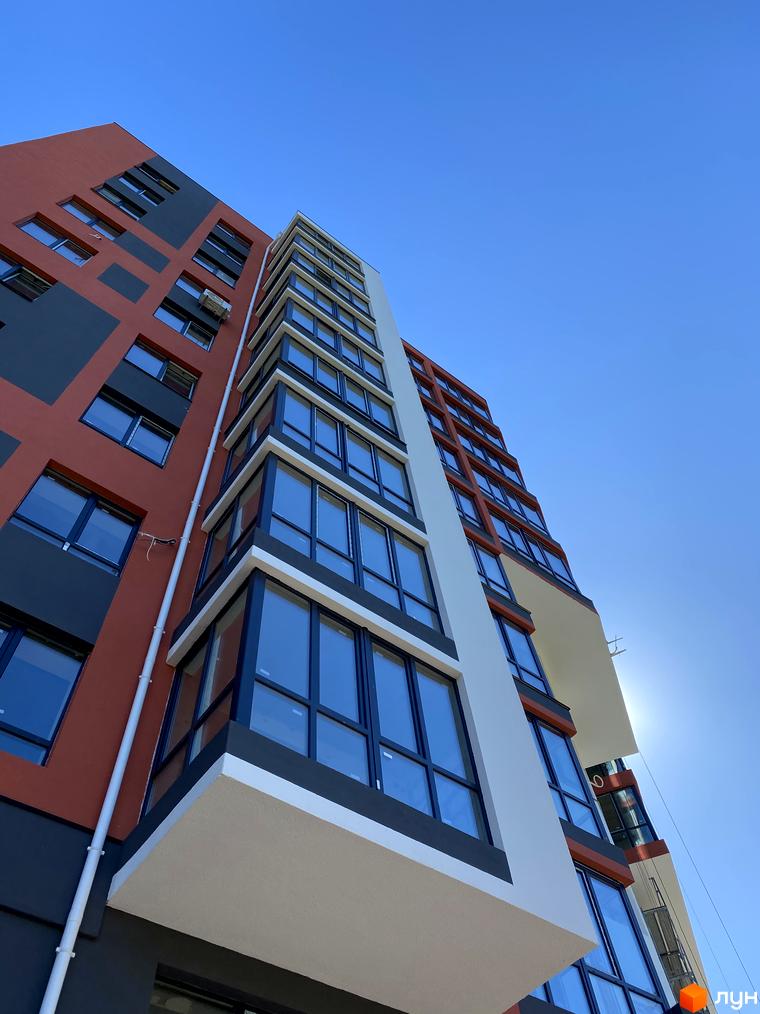 Зовнішній вигляд новобудови Green Life-3: багатоповерховий будинок з контрастним фасадом та панорамними вікнами під яскравим небом.