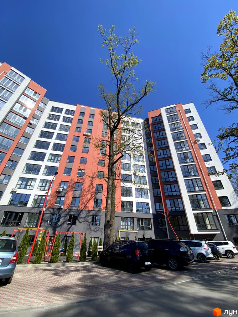 Фасад новобудови ЖК Green Life-3 з панорамними вікнами та балконами. Прибудинкова територія з дитячим майданчиком та парковкою.