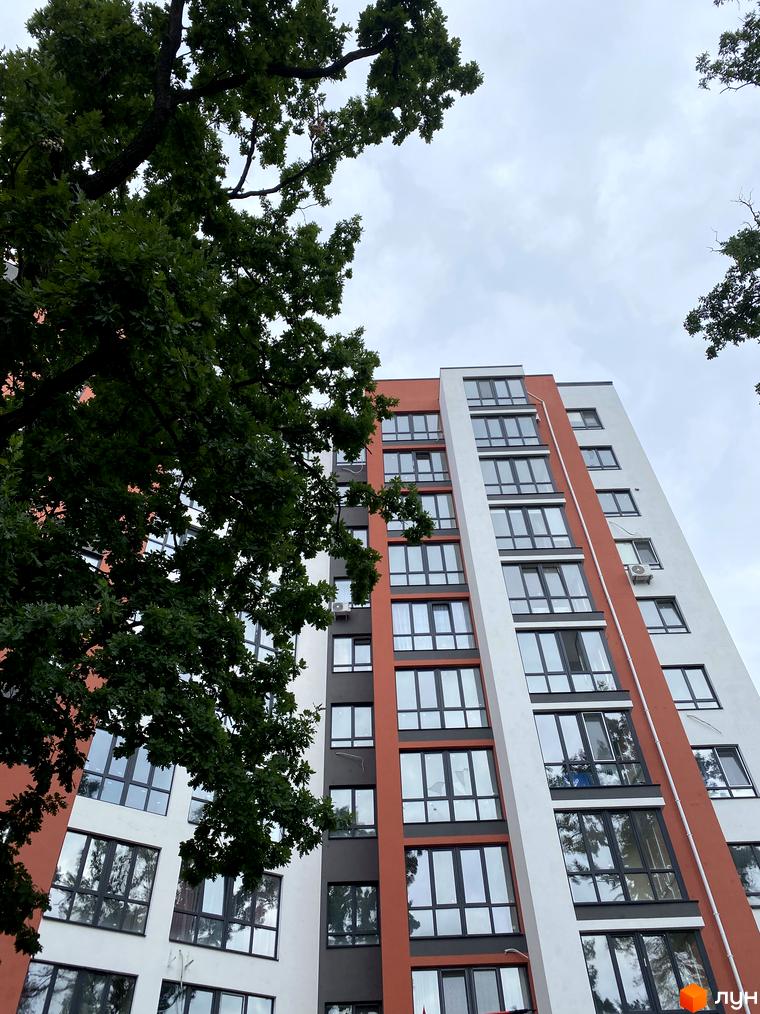 Житловий комплекс Green Life-3. Багатопоповерховий будинок з білими, помаранчево-червоними та темно-сірими фасадами, оточений зеленими деревами.