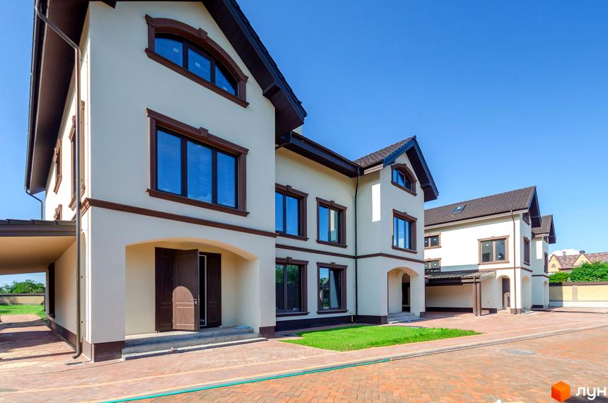 Котеджне містечко КМ Vita Energy residence з білою фасадною обробкою та коричневими віконними рамами. Навколо будівель розташована бруківка та зелений газон.