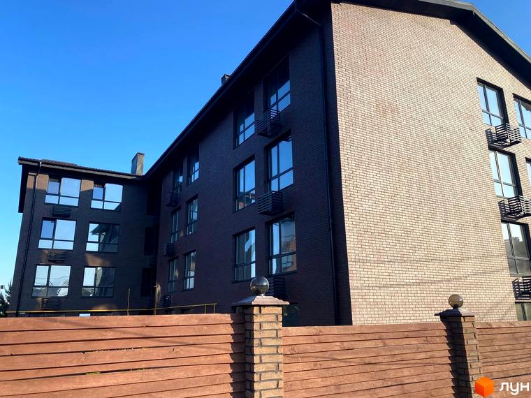 Зображення фасаду та вікон Житлового комплексу Моя Баварія. На передньому плані дерев'яний паркан.