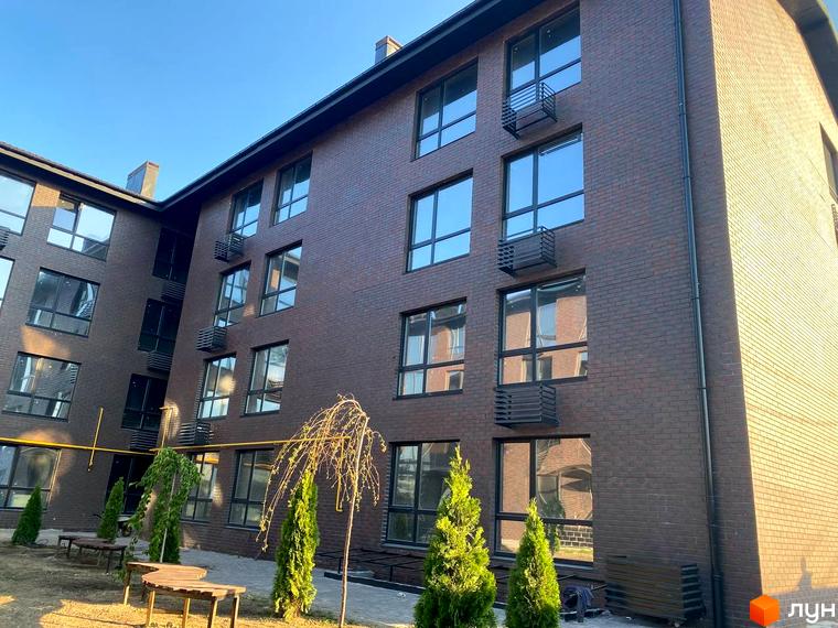 Зображення фасаду будинку Житлового комплексу Моя Баварія з великими вікнами та прибудинковою територією з деревами.