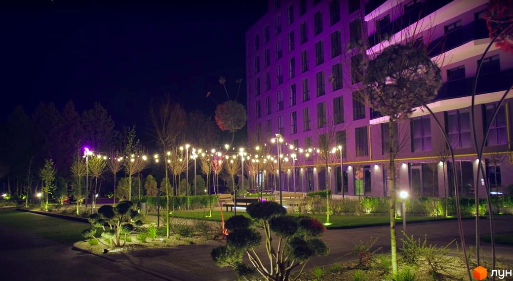 Житловий комплекс Tiffany з фіолетовою підсвіткою фасаду вночі. Прибудинкова територія освітлена гірляндами та ландшафтним освітленням.