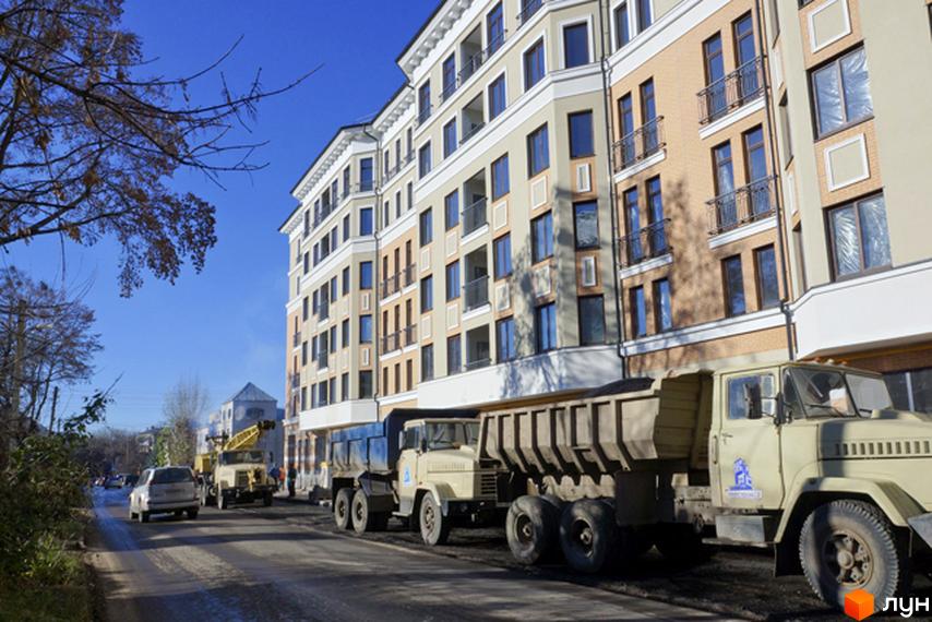 Житловий комплекс На Бакуліна. Багатоповерховий будинок з балконами та вікнами, поруч дорога з вантажівками та будівельною технікою.