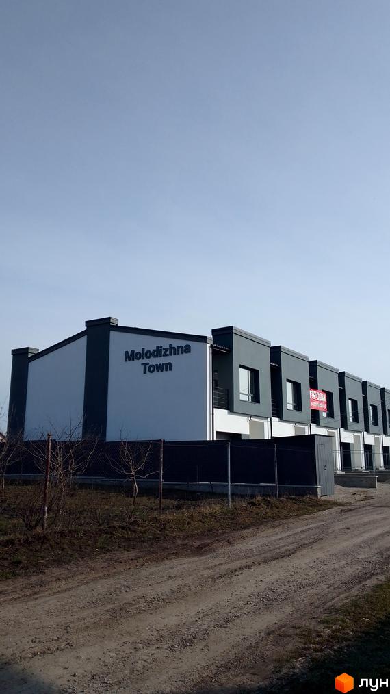 Зовнішній вигляд таунхаусів Molodizhna Town з фасадом з білої та сірої штукатурки, огородженою територією та дорогою.