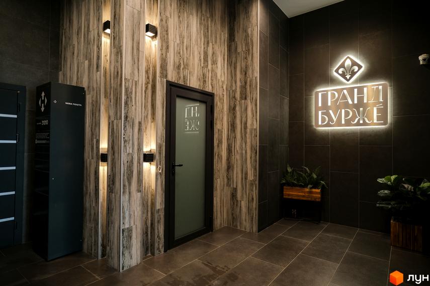 Лобі Житлового комплексу Гранд Бурже з оздобленням під дерево, темною плиткою та підсвіченою назвою. Встановлено поштомат Нова Пошта.