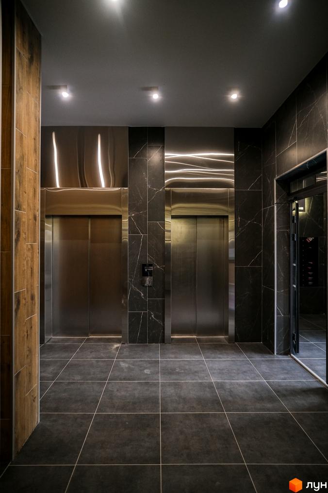 Інтер'єр ЖК Grand Bourget з ліфтами та темною плиткою на підлозі та стінах. Вигляд ліфтового холу в житловому комплексі.