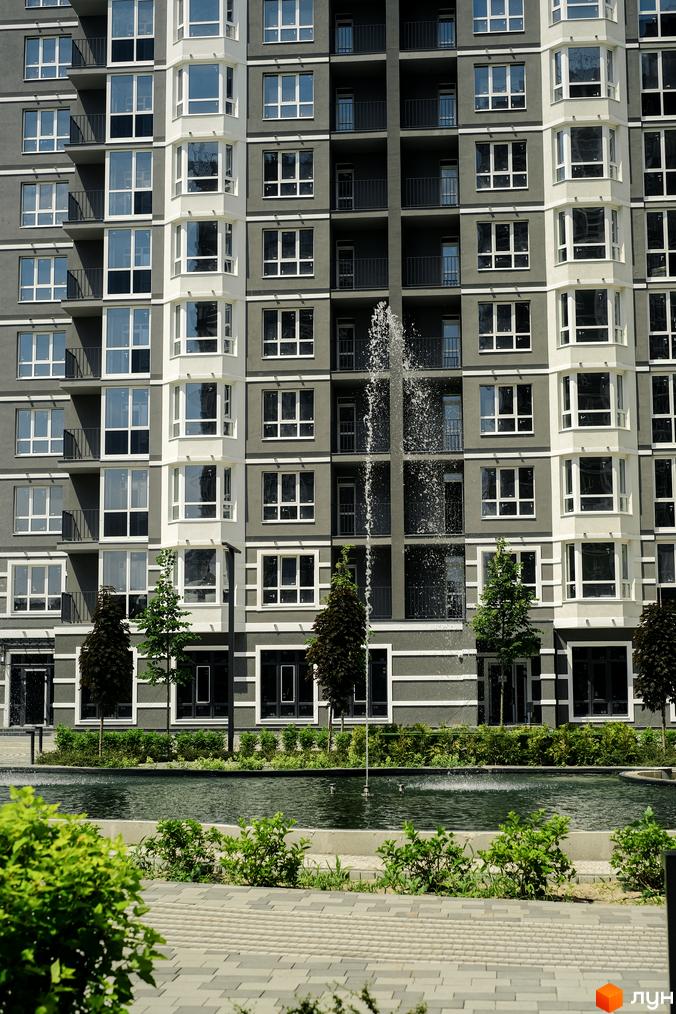 Фасад багатоповерхового будинку в Житловому комплексі Гранд Бурже. Прибудинкова територія з басейном та декоративними рослинами.