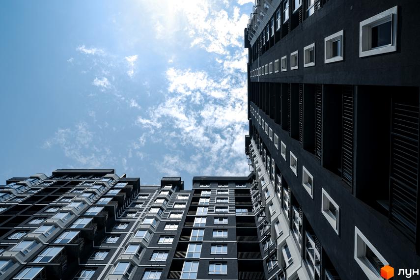 Високі житлові будинки Житлового комплексу Гранд Бурже з темним фасадом та білими вікнами на тлі блакитного неба з хмарами.