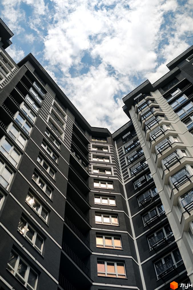 Вид знизу на висотний житловий комплекс Гранд Бурже з темно-сірим фасадом, білими горизонтальними та вертикальними лініями, та численними вікнами.