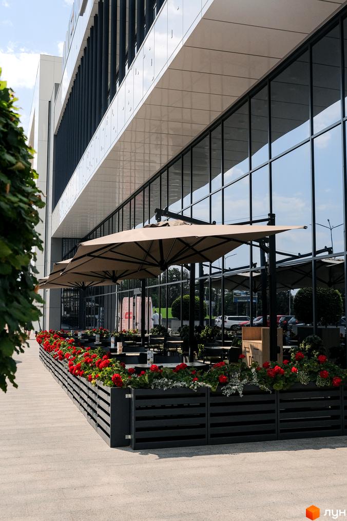 Зображення літнього майданчика біля Житлового комплексу Grand Bourget. Вигляд фасаду будівлі з великими вікнами та столиками для відвідувачів.
