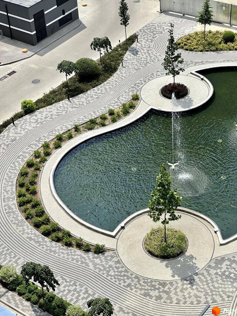 Житловий комплекс Гранд Бурже: темний будинок з горизонтальними смугами, великий ставок з фонтанами, мощені доріжки та зелені насадження.