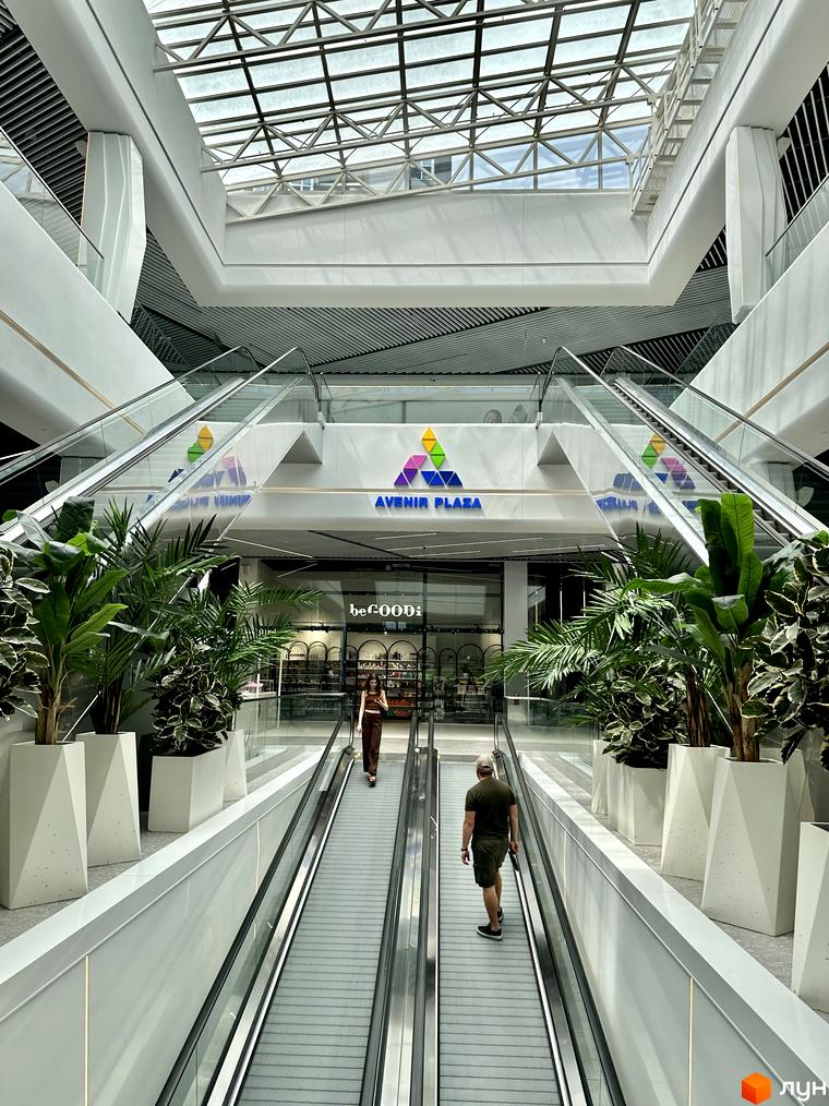 Просторий інтер'єр торгового центру AVENIR PLAZA з ескалаторами та великими рослинами, що є частиною інфраструктури Житлового комплексу Гранд Бурже.