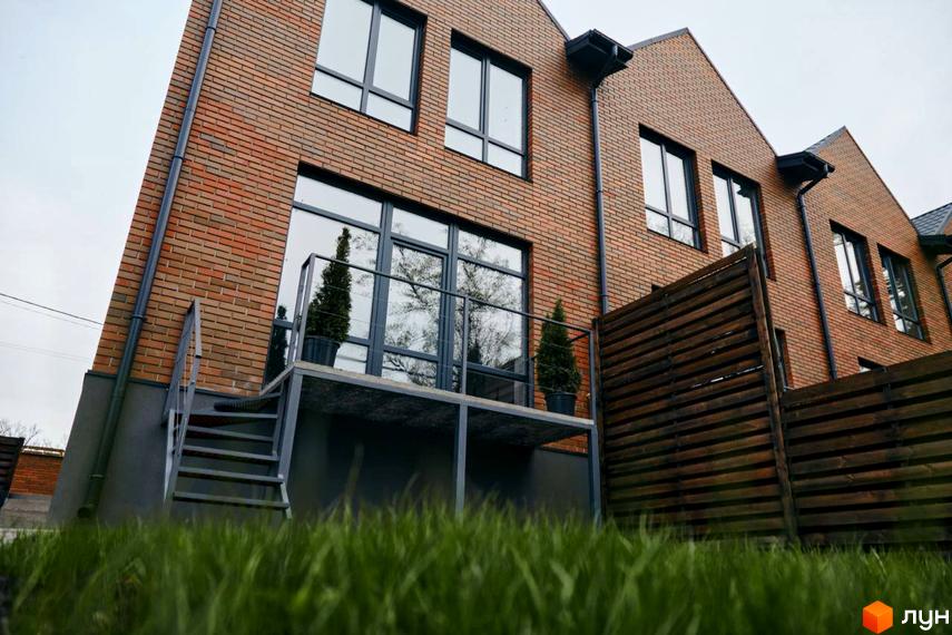 Зовнішній вигляд Котеджного містечка Positano Park з червоної цегли з великими вікнами та балконом. Навколо будинку зелений газон.