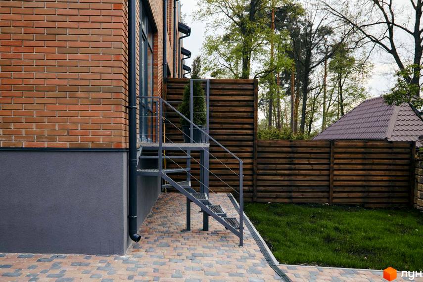 Вигляд фасаду будинку з червоної цегли в Котеджному містечку Positano Park. На подвір'ї викладена тротуарна плитка та зелений газон.