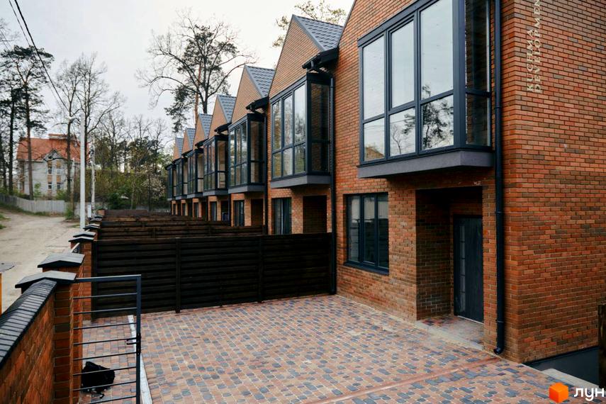 Вигляд на Котеджне містечко Positano Park з фасадом з червоної цегли та великими вікнами. На території викладена тротуарна плитка.