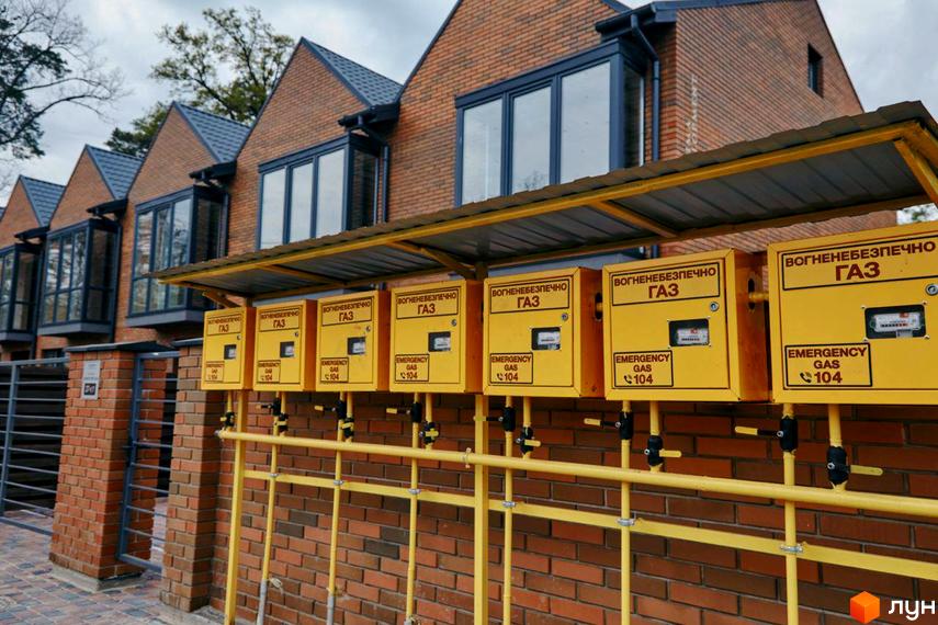 Фасад та прибудинкова територія Котеджного містечка Positano Park з газовими шафами вздовж цегляного паркану. Будинки з червоної цегли з темними дахами.