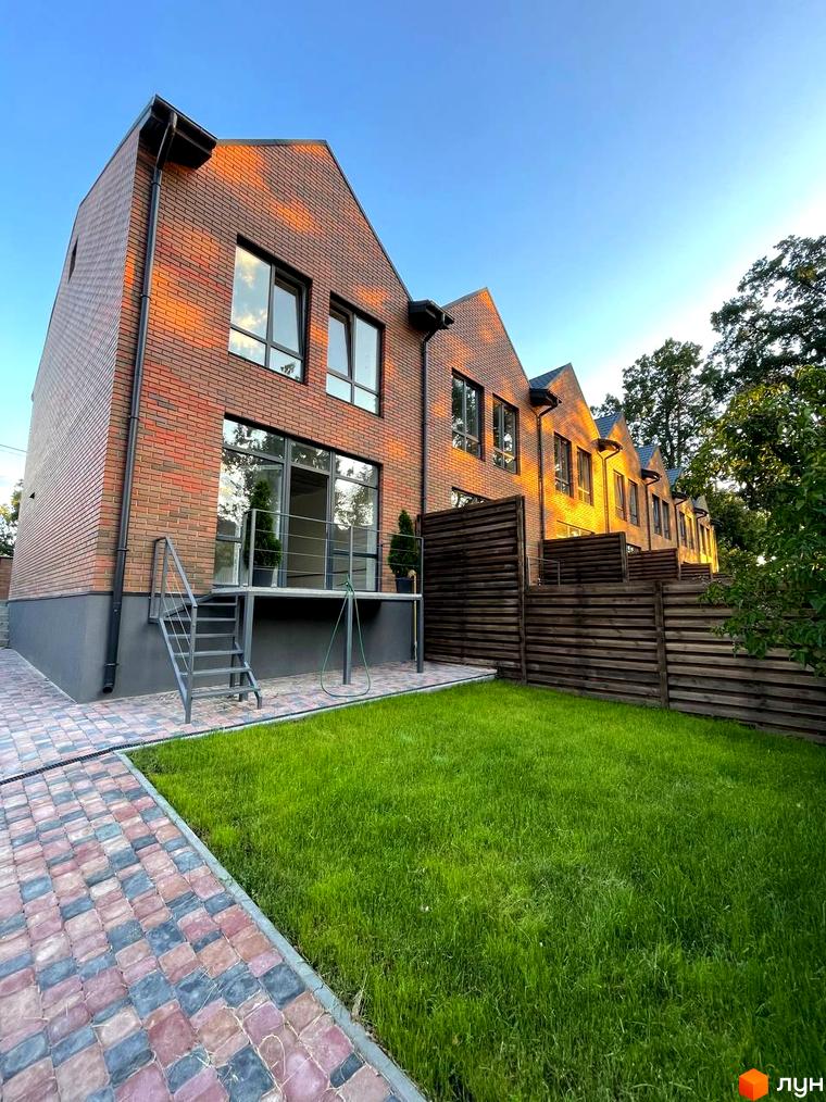 Зображення фасаду та прибудинкової території Котеджного містечка Positano Park. Вигляд будинку з газоном та доріжкою.