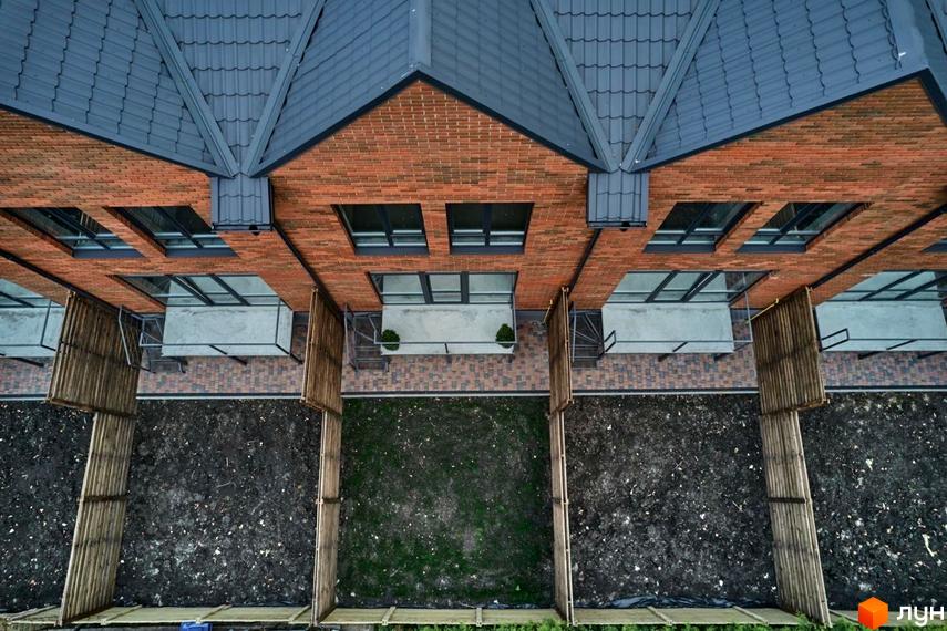 Вигляд зверху на цегляні таунхауси Котеджного містечка Positano Park з сірими дахами. Подвір'я з газоном та чорноземом, огороджені дерев'яним парканом.