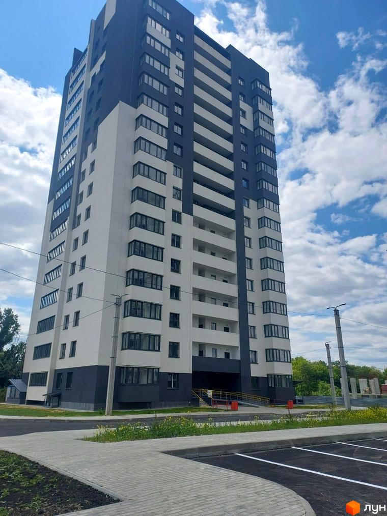 Житловий комплекс Оазис: багатоповерховий будинок з темно-сірим та білим фасадом, облаштована прибудинкова територія з парковкою.