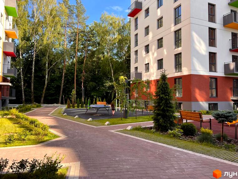 Житловий комплекс Проект Парк: багатоповерховий будинок з білим та червоним фасадом, оточений зеленим двором з деревами, доріжками та зоною відпочинку.