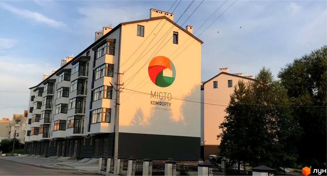 Житловий комплекс Місто Комфорту на Лісневицькій з білими фасадами, балконами та великим логотипом на торці. Поруч розташовані дерева та дорога.