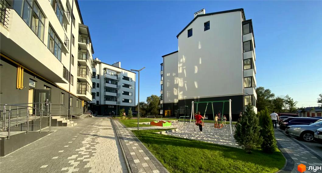 Житловий комплекс Місто Комфорту на Лісневицькій має світлі фасади з темними елементами та балконами. Прибудинкова територія облаштована доріжками, газонами та дитячим майданчиком.