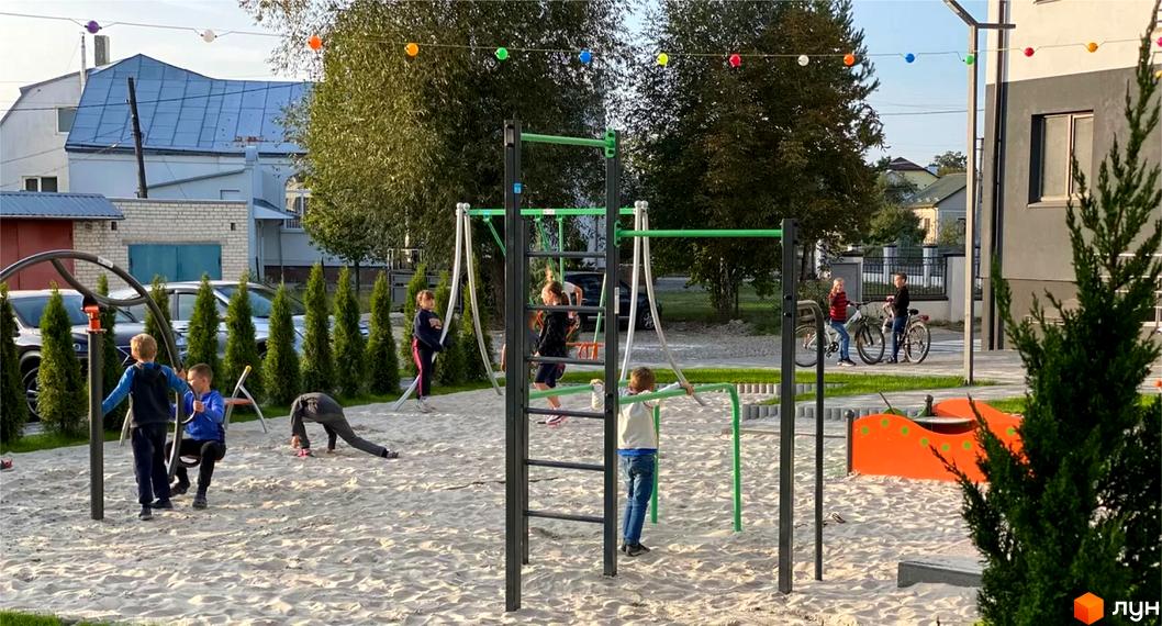 Житловий комплекс Місто Комфорту на Лісневицькій: фасад будинку сіро-білого кольору, поруч піщаний майданчик з ігровим обладнанням та дітьми.