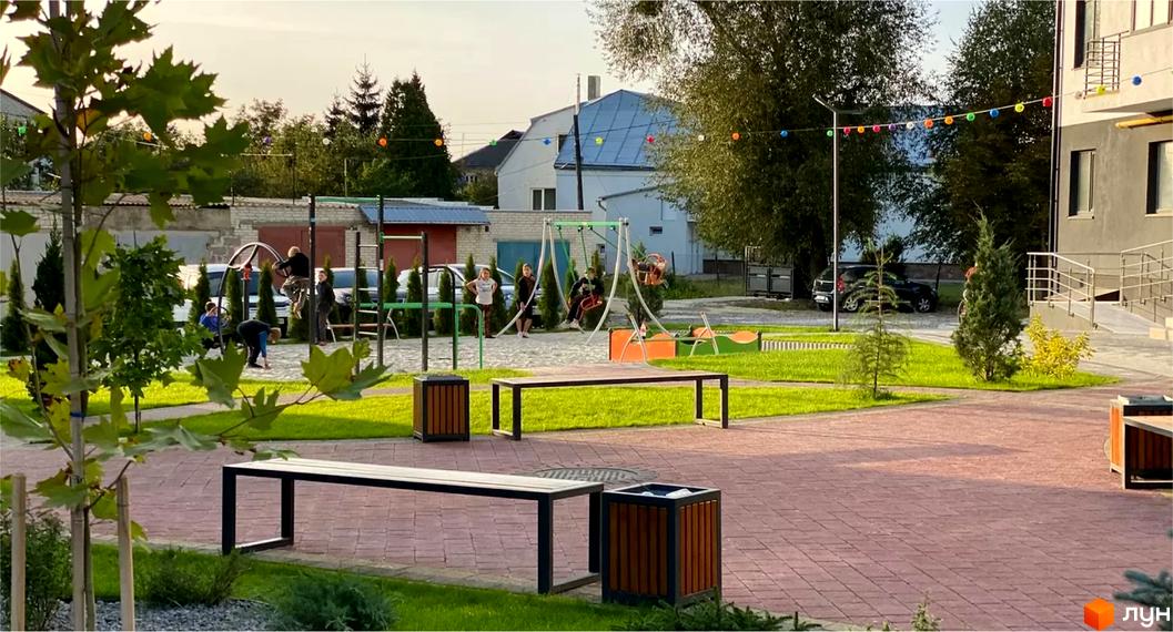 Фасад житлового комплексу Місто Комфорту на Лісневицькій з вікнами та балконами. На передньому плані дитячий майданчик з гойдалками та зеленими насадженнями.