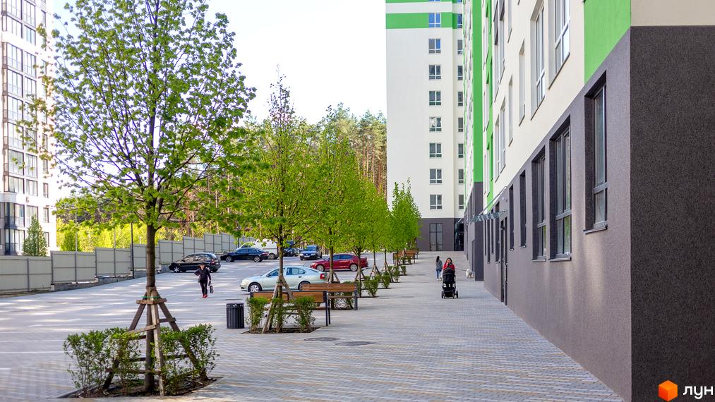 Зовнішній вигляд новобудови ЖК City Park з зеленими елементами та паркувальною зоною з деревами та лавками. На території комплексу розташовані автомобілі та пішохідні доріжки.