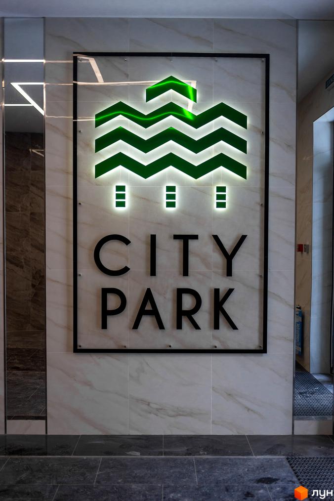 Логотип житлового комплексу City Park з зеленим логотипом та назвою. Зовнішній вигляд фасаду будинку з мармуровою плиткою та підсвіткою.