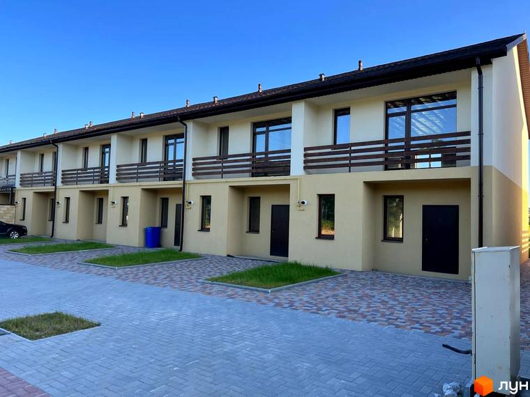 Таунхаус „Європейський“: ряд двоповерхових будівель бежевого кольору з балконами. Перед будинками бруковані доріжки та газони.