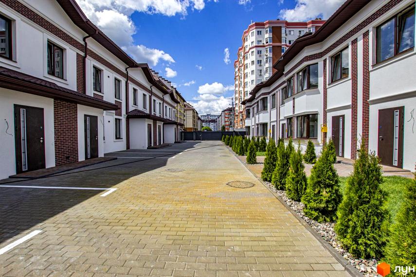 Таунхауси на Львівському: фасади будинків з цегляними елементами та білою штукатуркою, доглянута прибудинкова територія з туями та бруківкою.