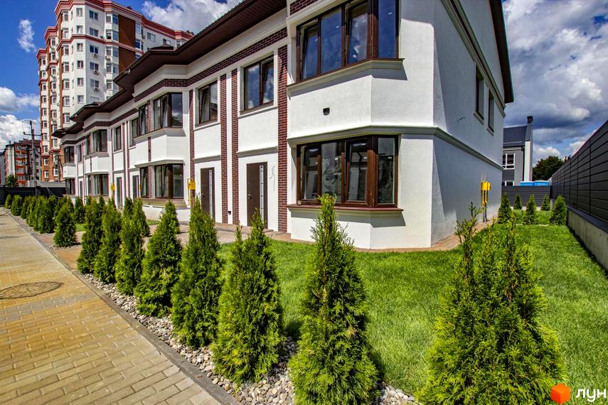 Таунхауси на Львівському - фасади білої штукатурки з цегляними вставками та коричневими вікнами, зелений газон та туї біля доріжки.
