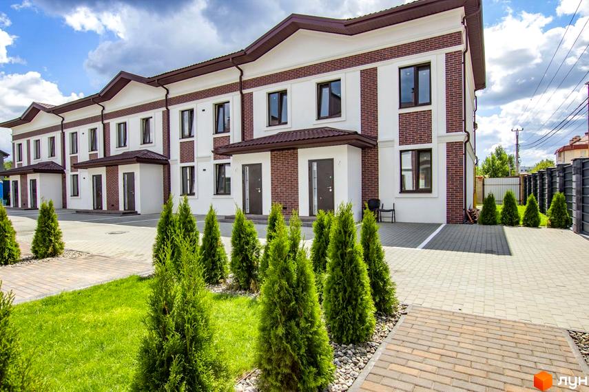 Таунхауси на Львівському: фасади з білою та цегляною обробкою, двоповерхові будівлі з коричневими дахами, зелені туї та бруківка на прибудинковій території.