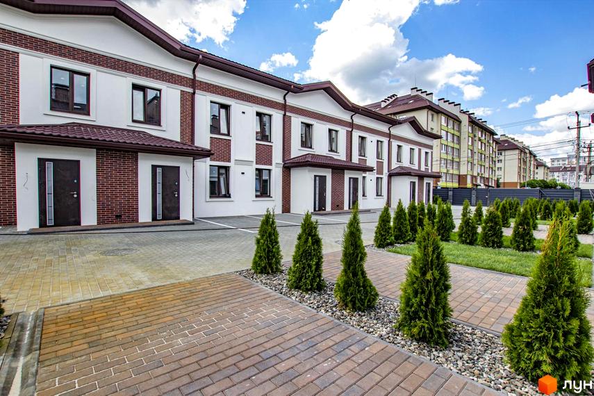 Зовнішній вигляд таунхаусів на Львівському: білі фасади з цегляними елементами та коричневими дахами. Прибудинкова територія з акуратними туями та бруківкою.