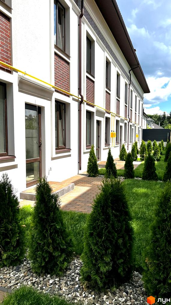 Таунхауси на Львівському: білий фасад з коричневими вікнами та цегляними вставками, зелені туї та доглянутий газон. Комплекс з індивідуальним опаленням та газовим підведенням.