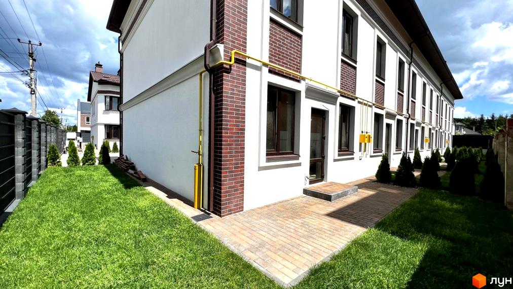 Таунхауси на Львівському: білий фасад з цегляними вставками, коричневі вікна, бруківка та зелений газон. Зовнішній вигляд новобудови.
